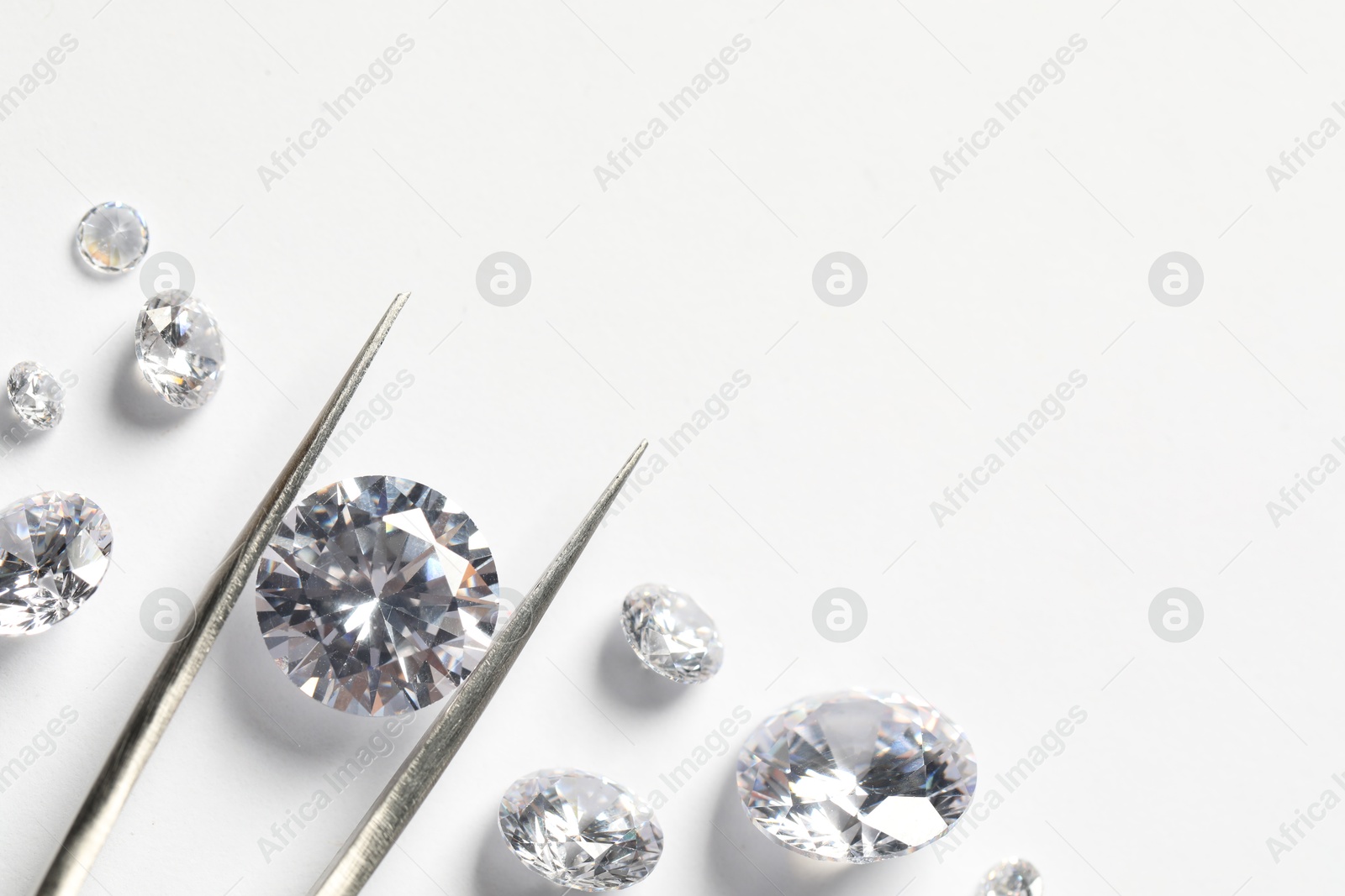 Photo of Many beautiful shiny diamonds and tweezers on white background, flat lay. Space for text