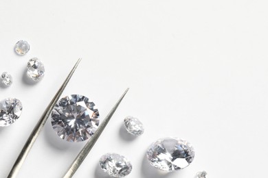 Many beautiful shiny diamonds and tweezers on white background, flat lay. Space for text