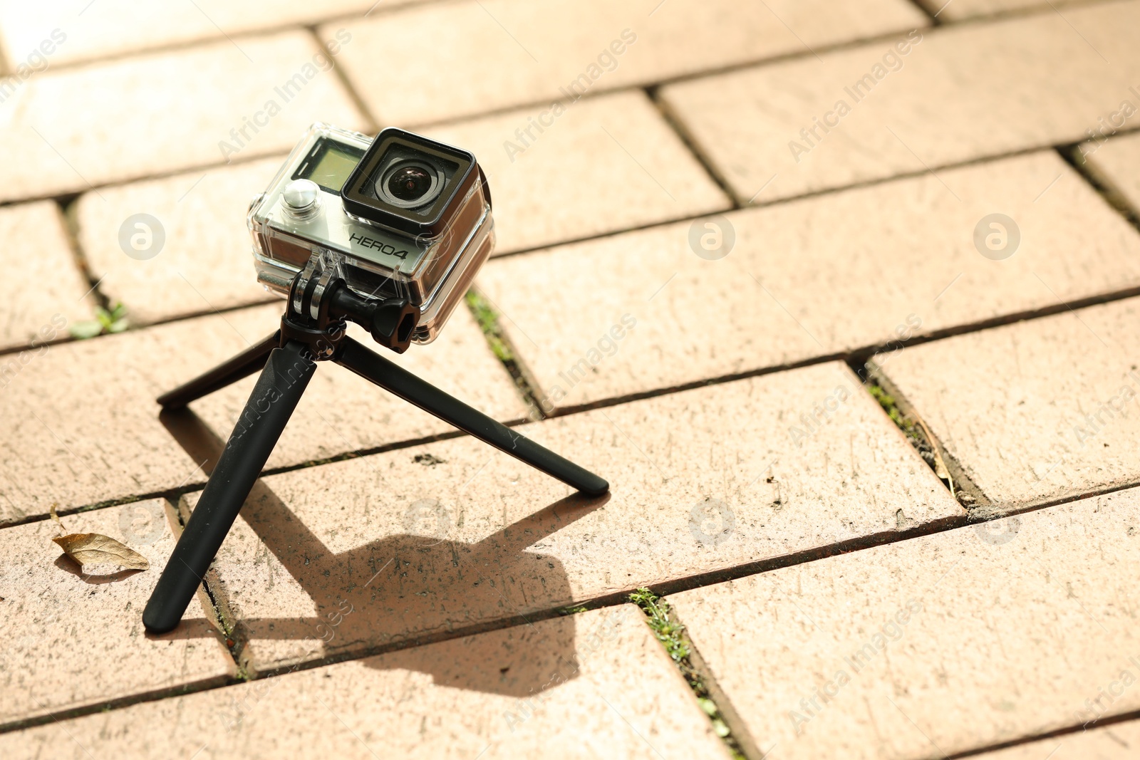 Photo of Modern action camera with tripod on pavement outdoors, space for text