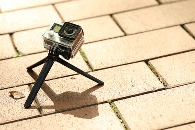 Modern action camera with tripod on pavement outdoors, space for text