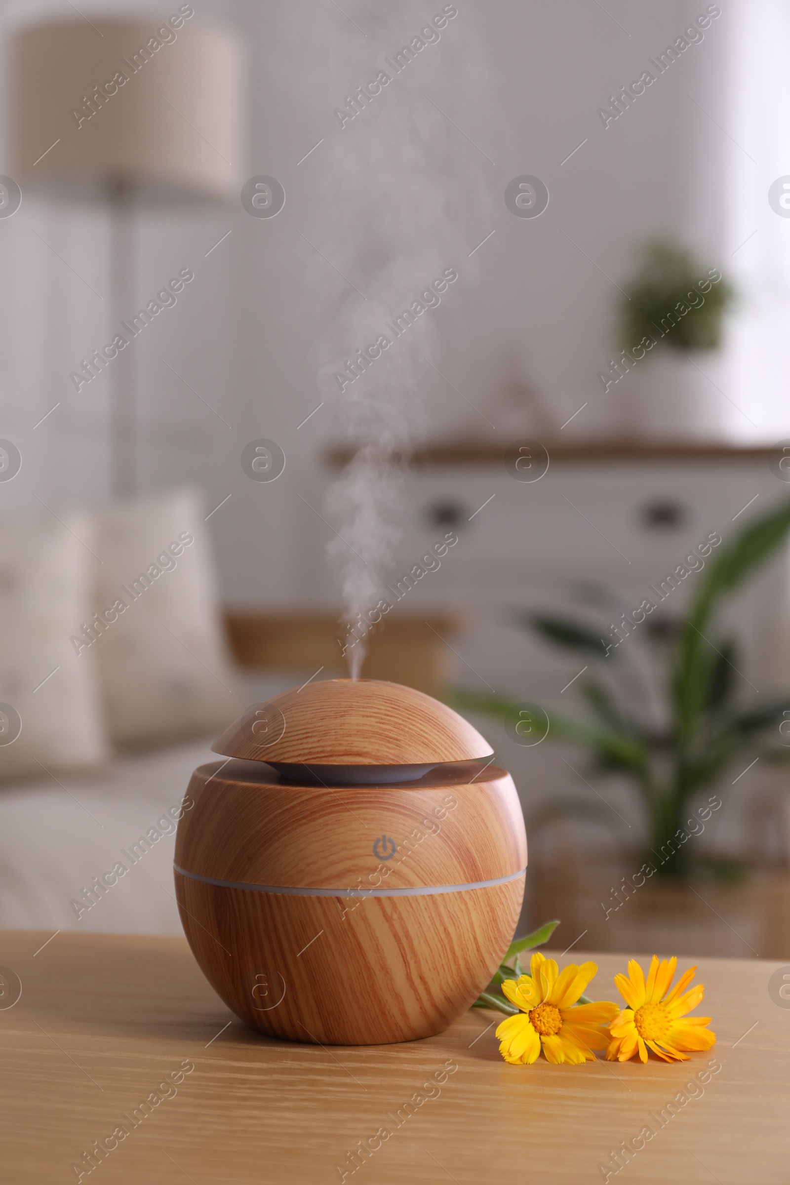 Photo of Essential oil diffuser and calendula flowers on wooden table at home