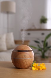 Photo of Essential oil diffuser and calendula flowers on wooden table at home