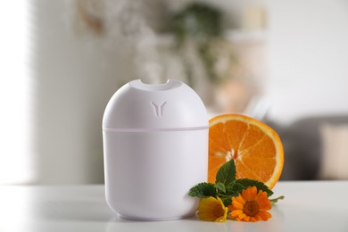 Photo of Essential oil diffuser, calendula flowers, mint and orange on white table at home