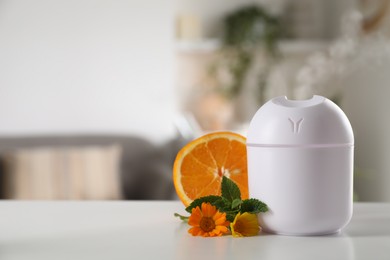 Photo of Essential oil diffuser, calendula flowers, mint and orange on white table at home, space for text