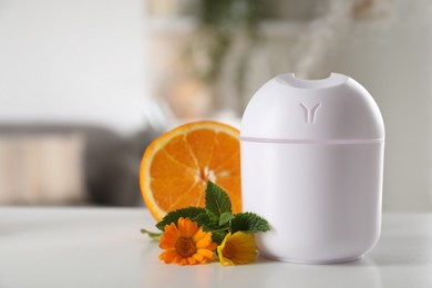 Photo of Essential oil diffuser, calendula flowers, mint and orange on white table at home. Space for text