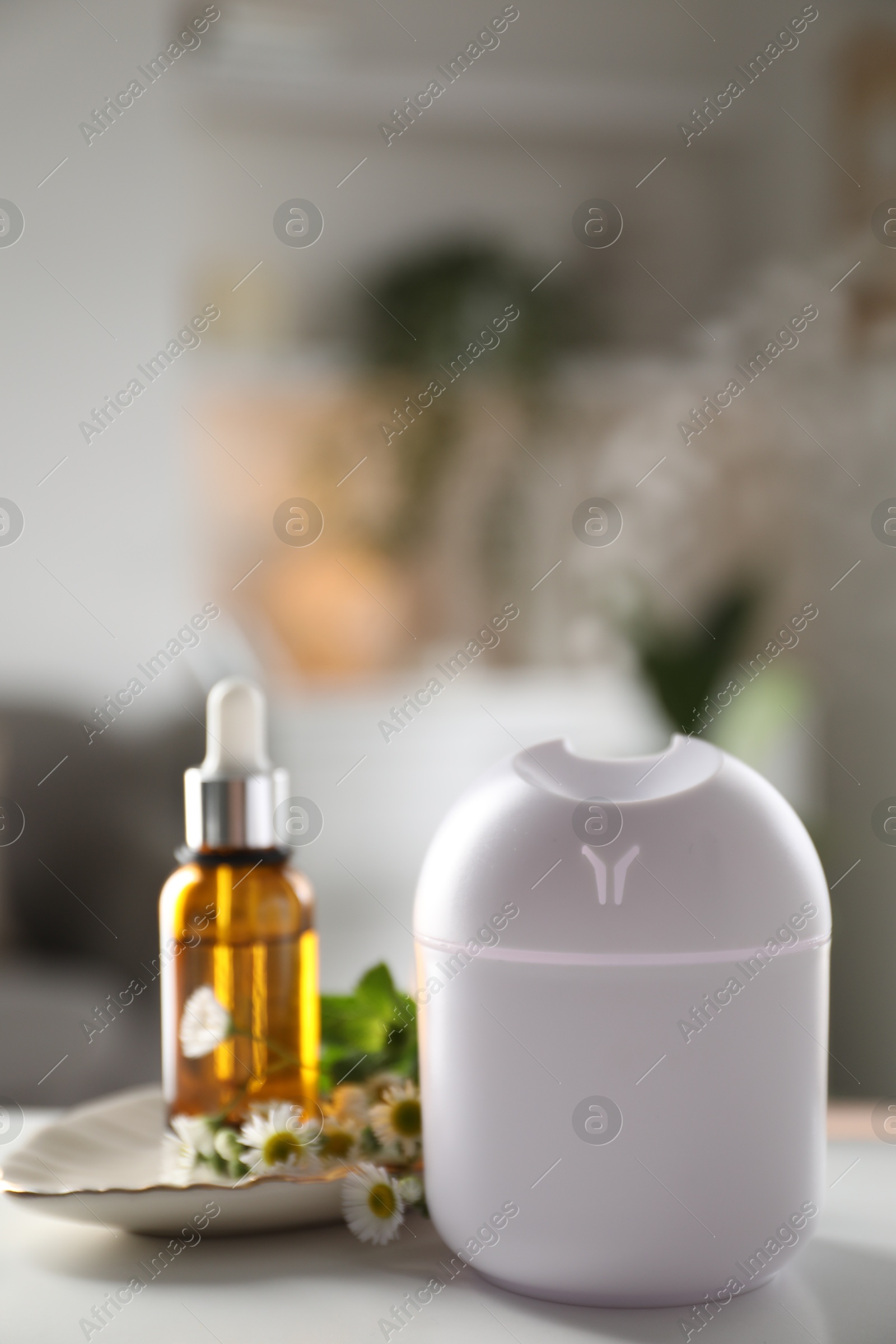 Photo of Essential oil diffuser, cosmetic product and chamomile flowers on white table at home