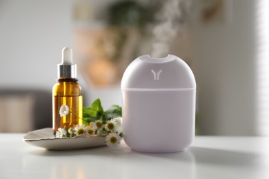 Photo of Essential oil diffuser, cosmetic product and chamomile flowers on white table at home