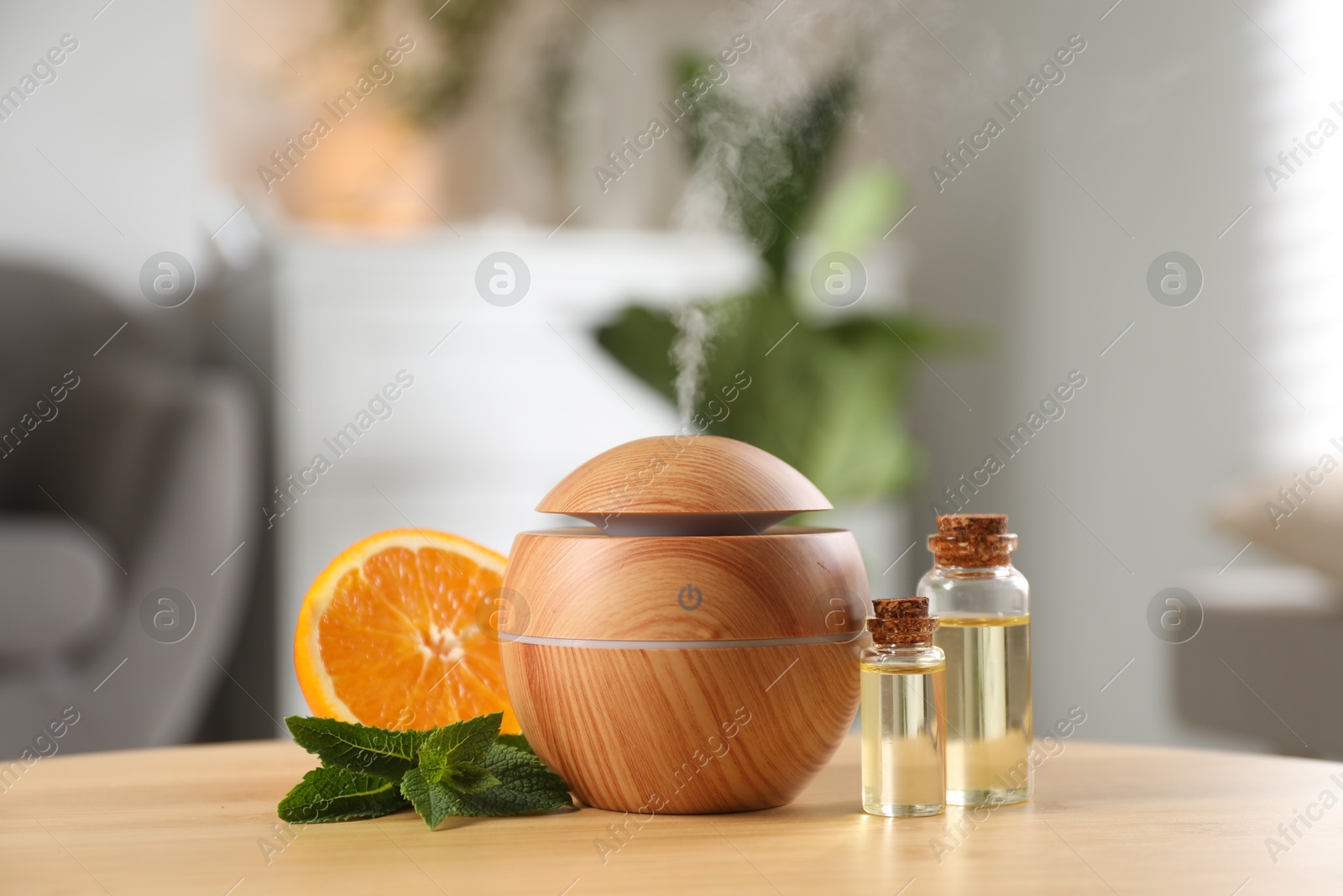 Photo of Essential oil diffuser, cosmetic products, mint and orange on wooden table at home