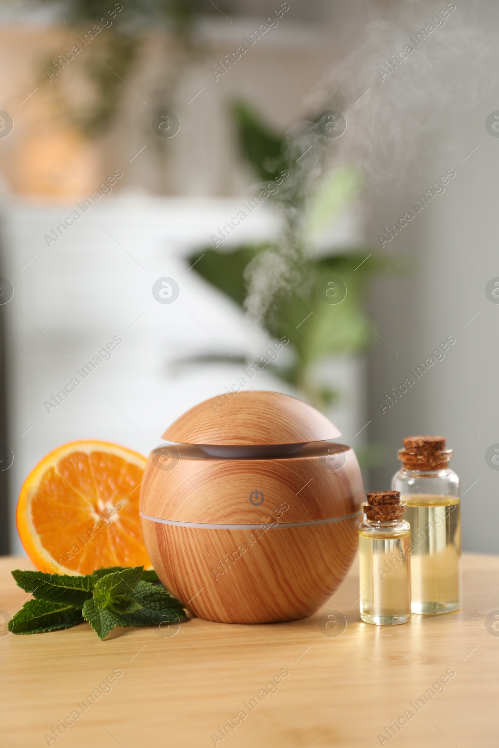 Photo of Essential oil diffuser, cosmetic products, mint and orange on wooden table at home