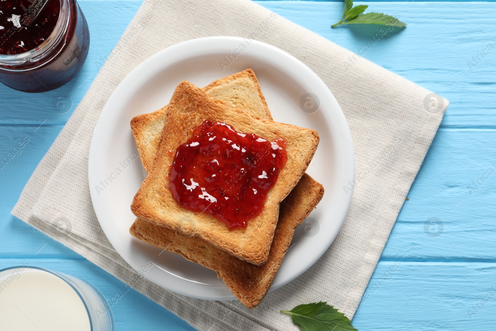 Photo of Delicious toasts with jam and milk on light blue wooden table, flat lay