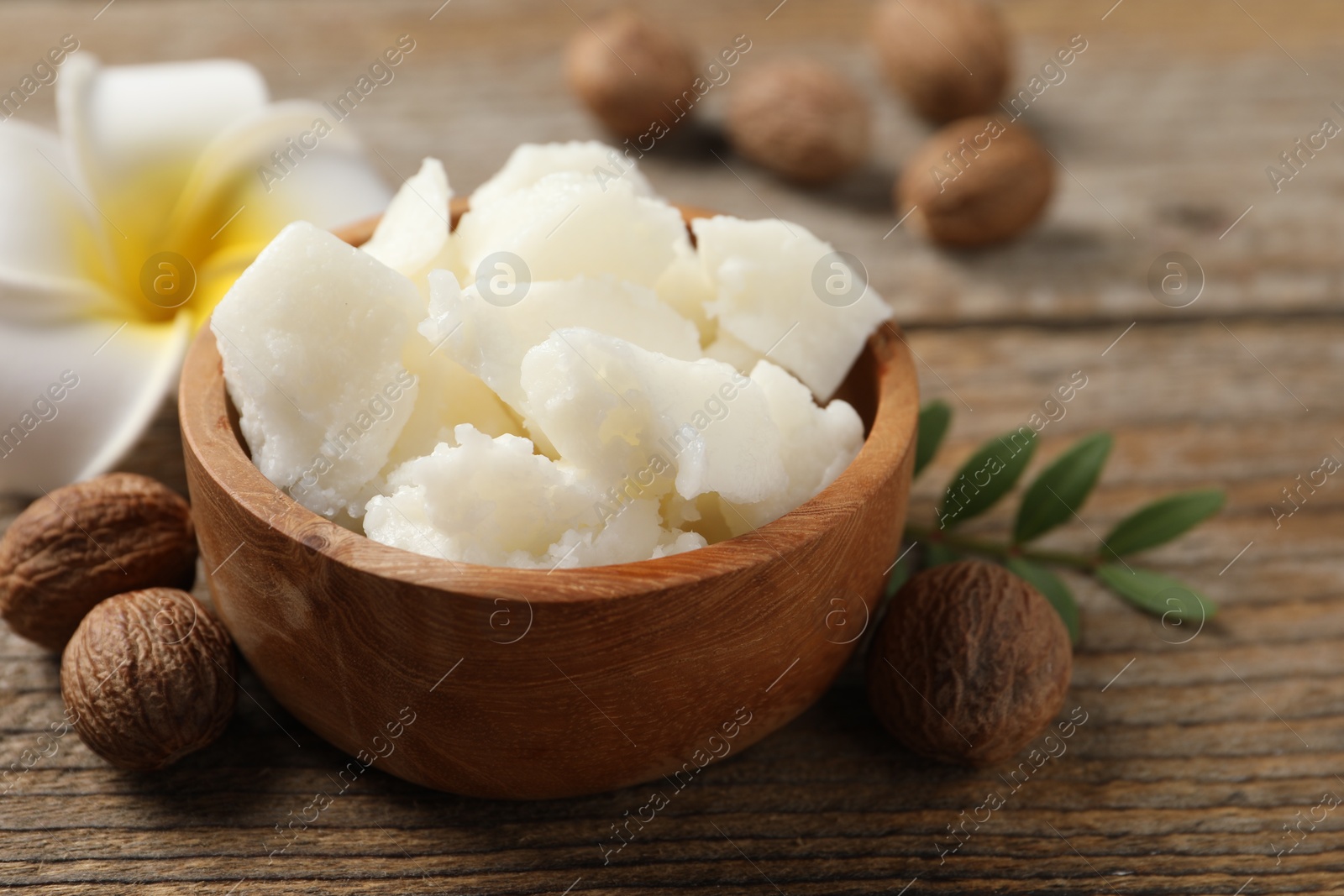 Photo of Natural shea butter, nuts and plumeria flower on wooden table, closeup