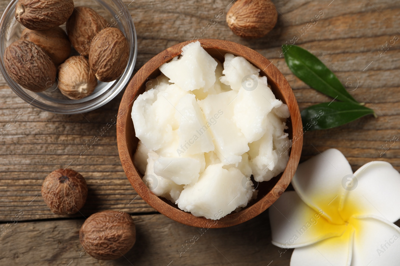 Photo of Natural shea butter, nuts and plumeria flower on wooden table, flat lay