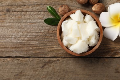 Photo of Natural shea butter, nuts and plumeria flower on wooden table, flat lay. Space for text