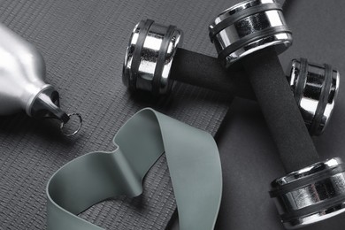 Dumbbells, yoga mat, thermo bottle and fitness elastic band on black background, above view