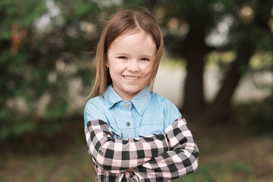 Portrait of happy little girl with crossed arms outdoors