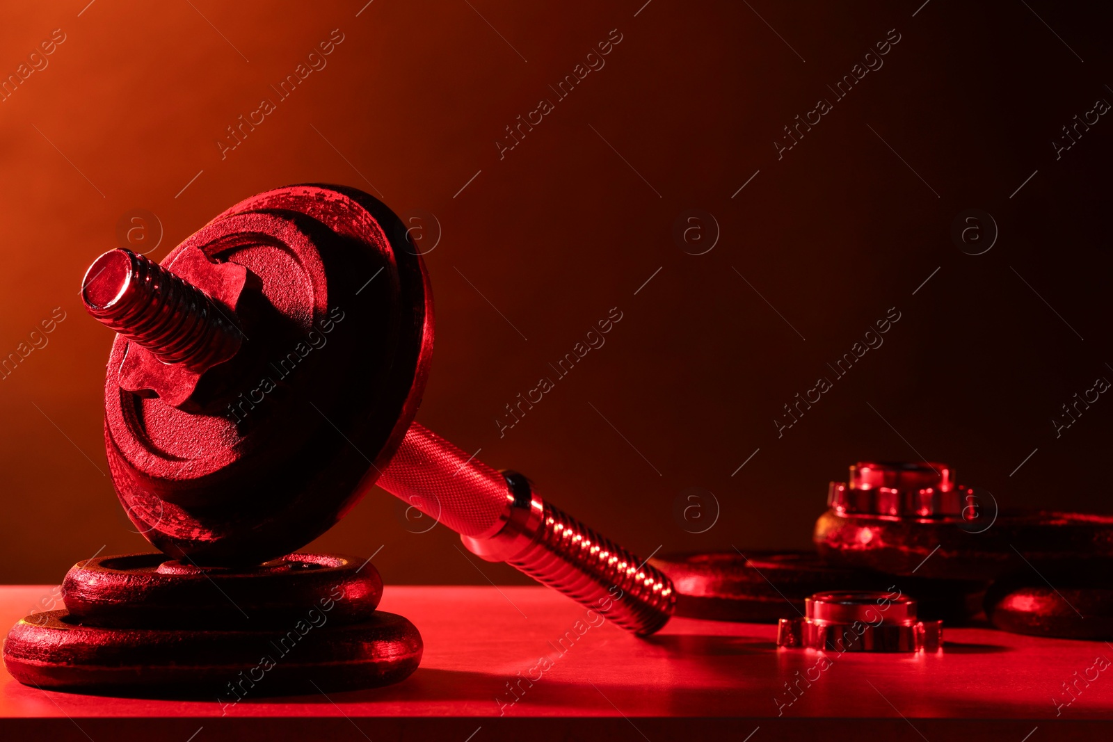 Photo of Parts of barbell on table in color lights. Space for text