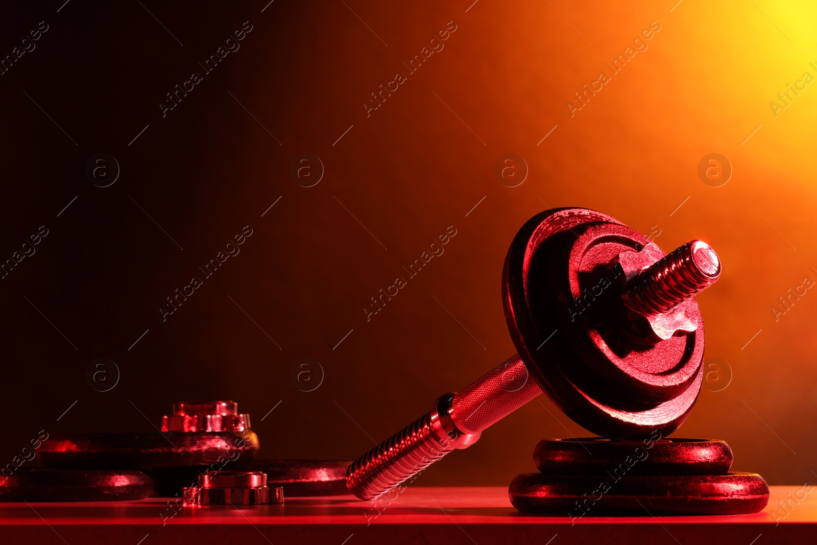 Photo of Parts of barbell on table in color lights. Space for text