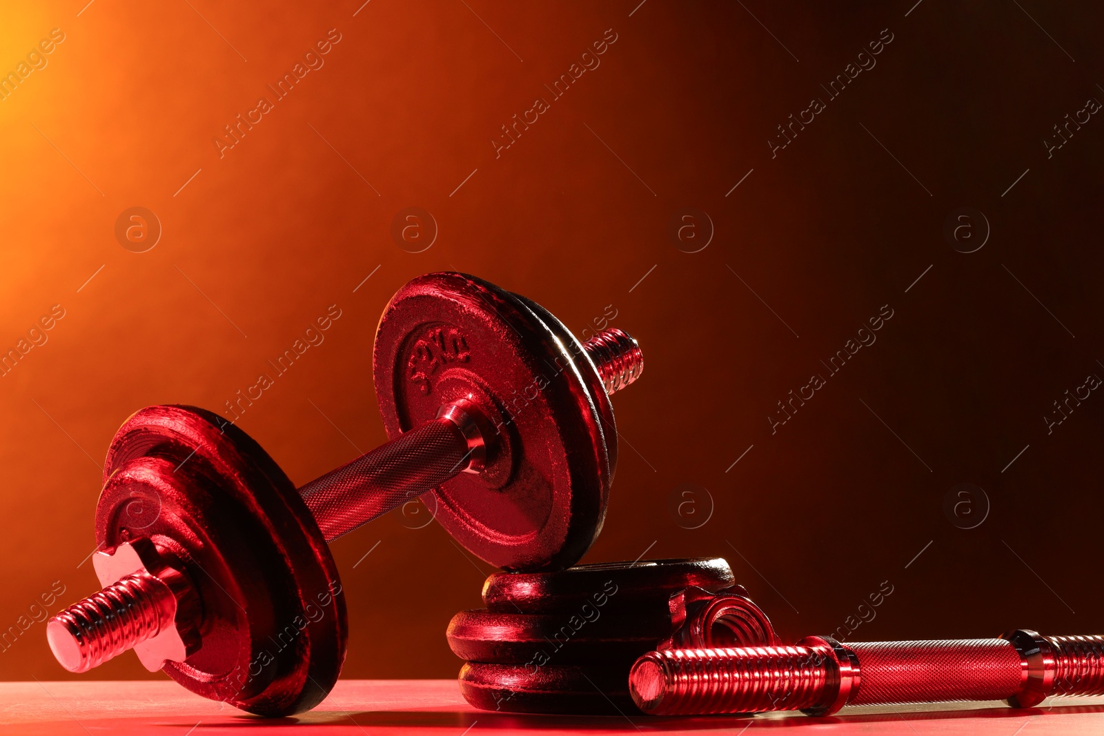 Photo of Barbell and parts of one on table in color lights. Space for text