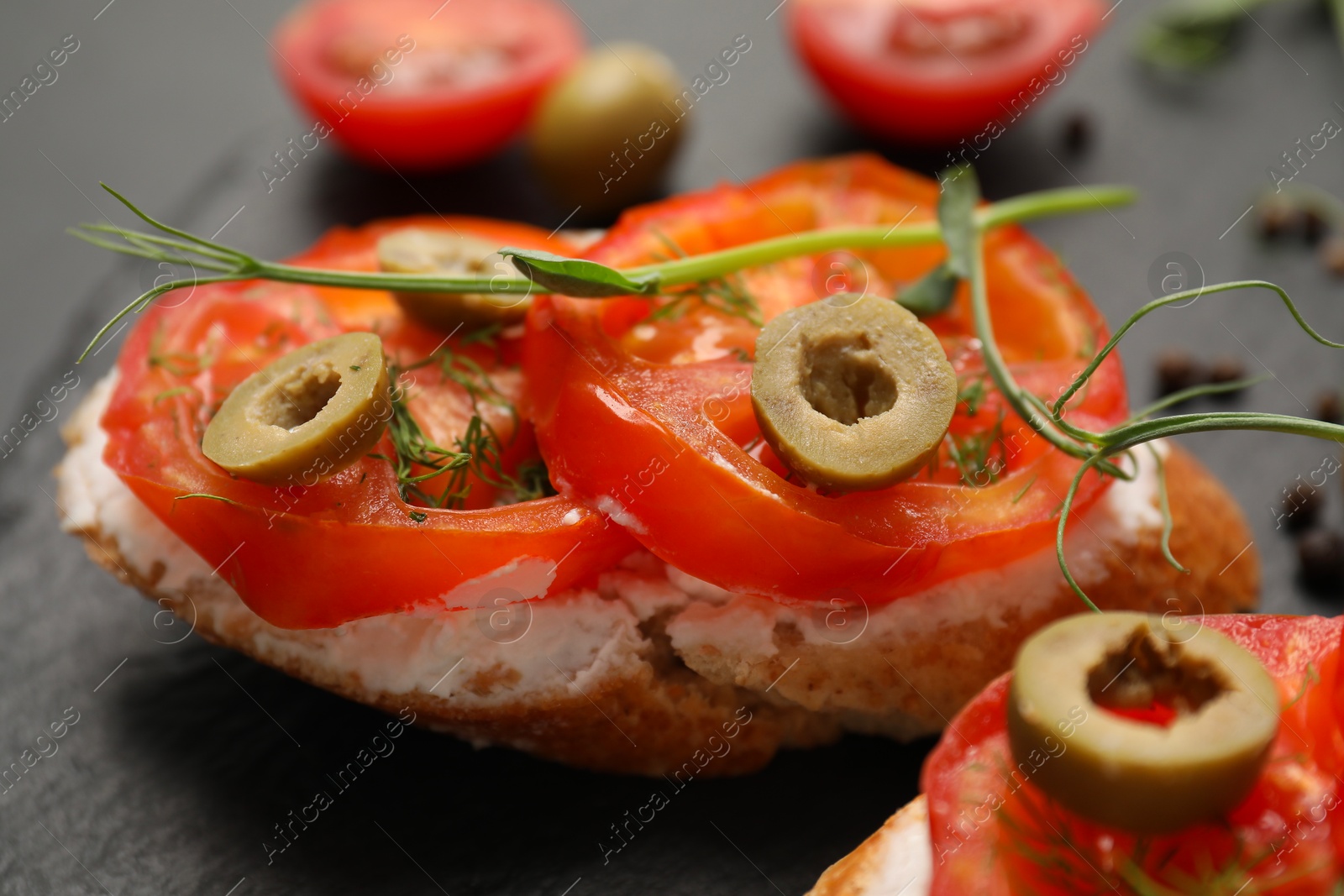 Photo of Delicious ricotta bruschettas with sliced tomatoes, olives and greens on black table, closeup