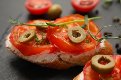 Delicious ricotta bruschettas with sliced tomatoes, olives and greens on black table, closeup