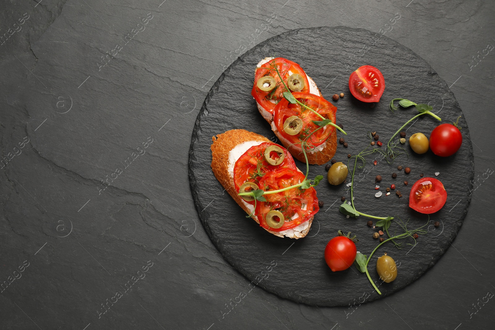 Photo of Delicious ricotta bruschettas with sliced tomatoes, olives and greens on black table, top view. Space for text