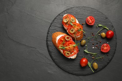 Delicious ricotta bruschettas with sliced tomatoes, olives and greens on black table, top view. Space for text