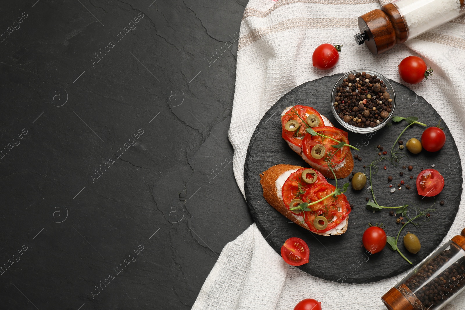 Photo of Delicious ricotta bruschettas with sliced tomatoes, olives and greens on black table, top view. Space for text