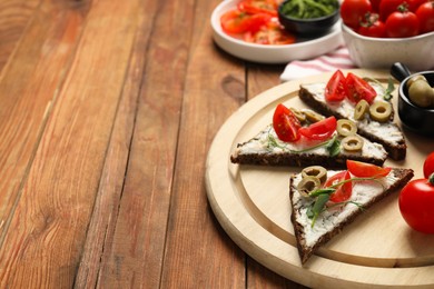 Delicious ricotta bruschettas with fresh tomatoes, olives and greens on wooden table. Space for text