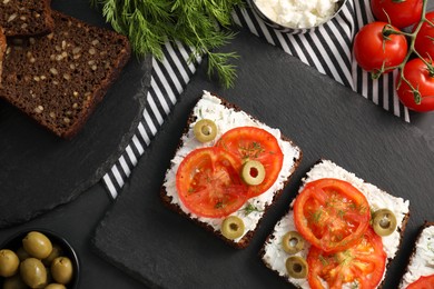 Delicious ricotta bruschettas with sliced tomatoes, olives and greens on black table, flat lay