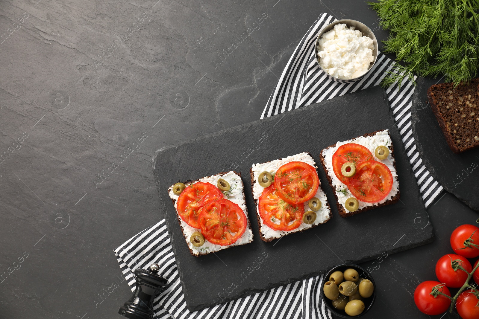 Photo of Delicious ricotta bruschettas with sliced tomatoes, olives and greens on black table. Space for text