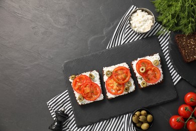 Delicious ricotta bruschettas with sliced tomatoes, olives and greens on black table. Space for text