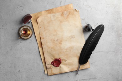 Photo of Sheet of old parchment paper with wax stamp, black feather, inkwell and candle on grey table, flat lay