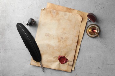 Photo of Sheet of old parchment paper with wax stamp, black feather, inkwell and candle on grey table, flat lay