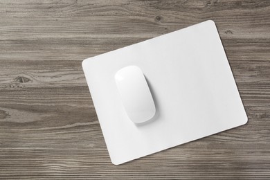 Wireless mouse and mousepad on wooden table, top view. Space for text