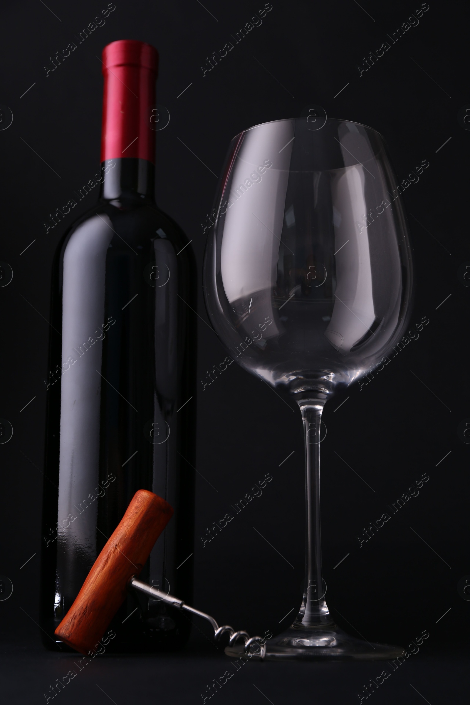 Photo of Bottle of wine, corkscrew and glass on dark background