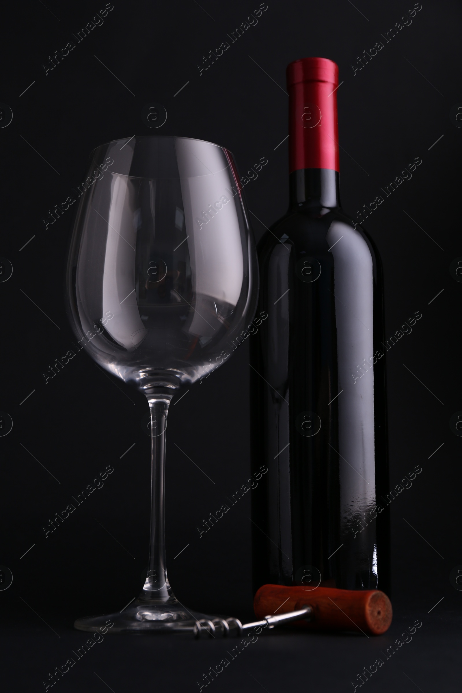 Photo of Bottle of wine, corkscrew and glass on dark background