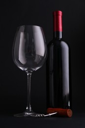 Bottle of wine, corkscrew and glass on dark background