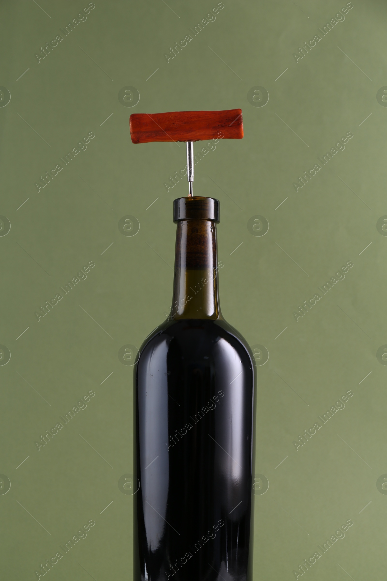 Photo of Wine bottle with corkscrew on olive background