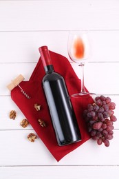 Corkscrew, bottle of wine, glass, walnuts and grapes on white wooden table, top view