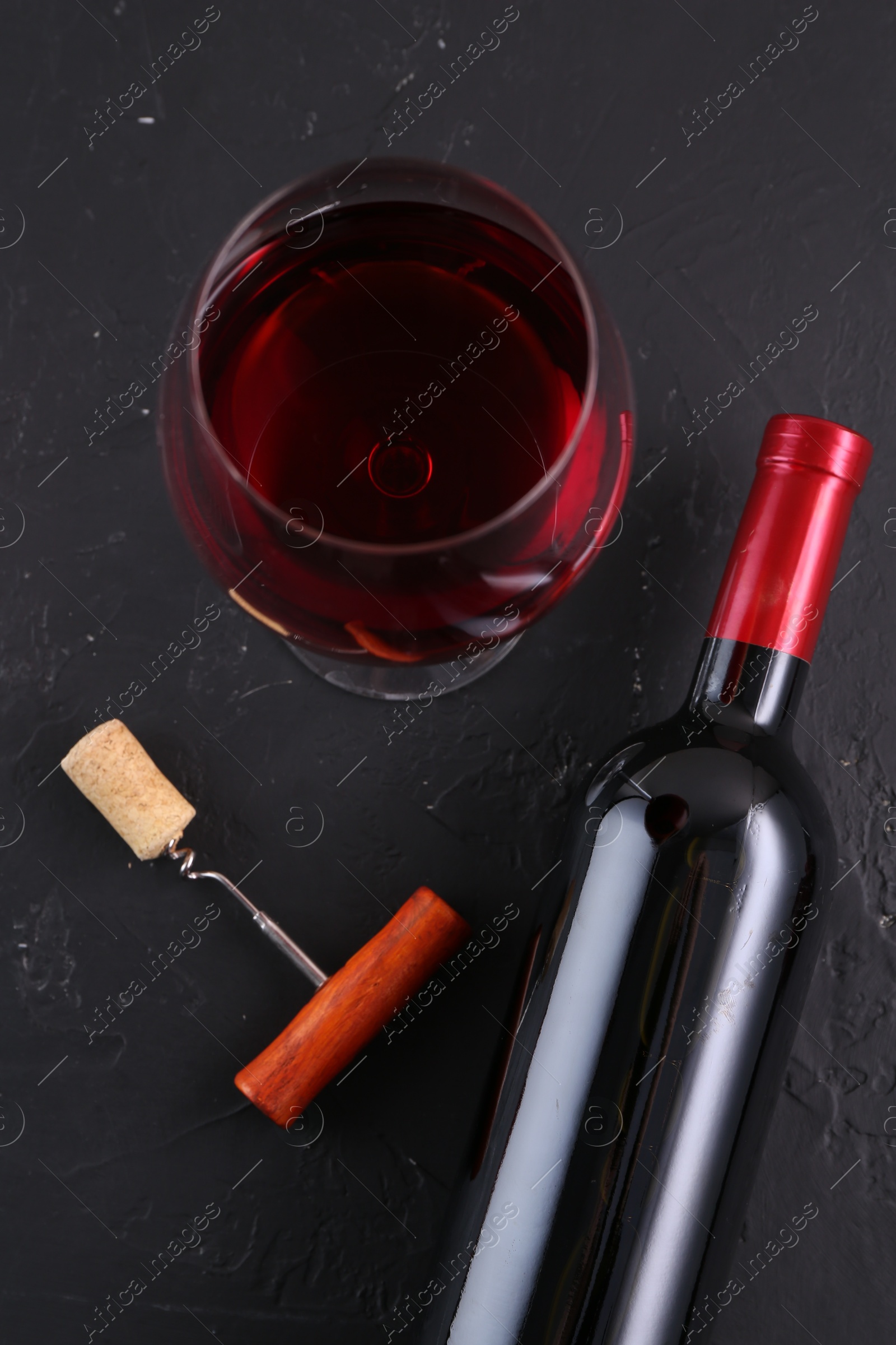 Photo of Corkscrew, glass of wine and bottle on black table, flat lay