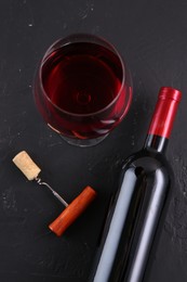 Photo of Corkscrew, glass of wine and bottle on black table, flat lay