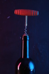 Photo of Wine bottle with corkscrew in lights on dark background