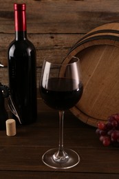 Glass of wine, bottle, barrel and grapes on wooden table