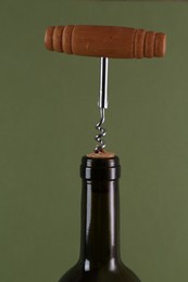 Wine bottle with corkscrew on olive background, closeup