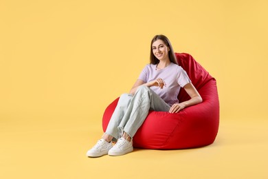 Photo of Smiling woman sitting on red bean bag chair against yellow background, space for text