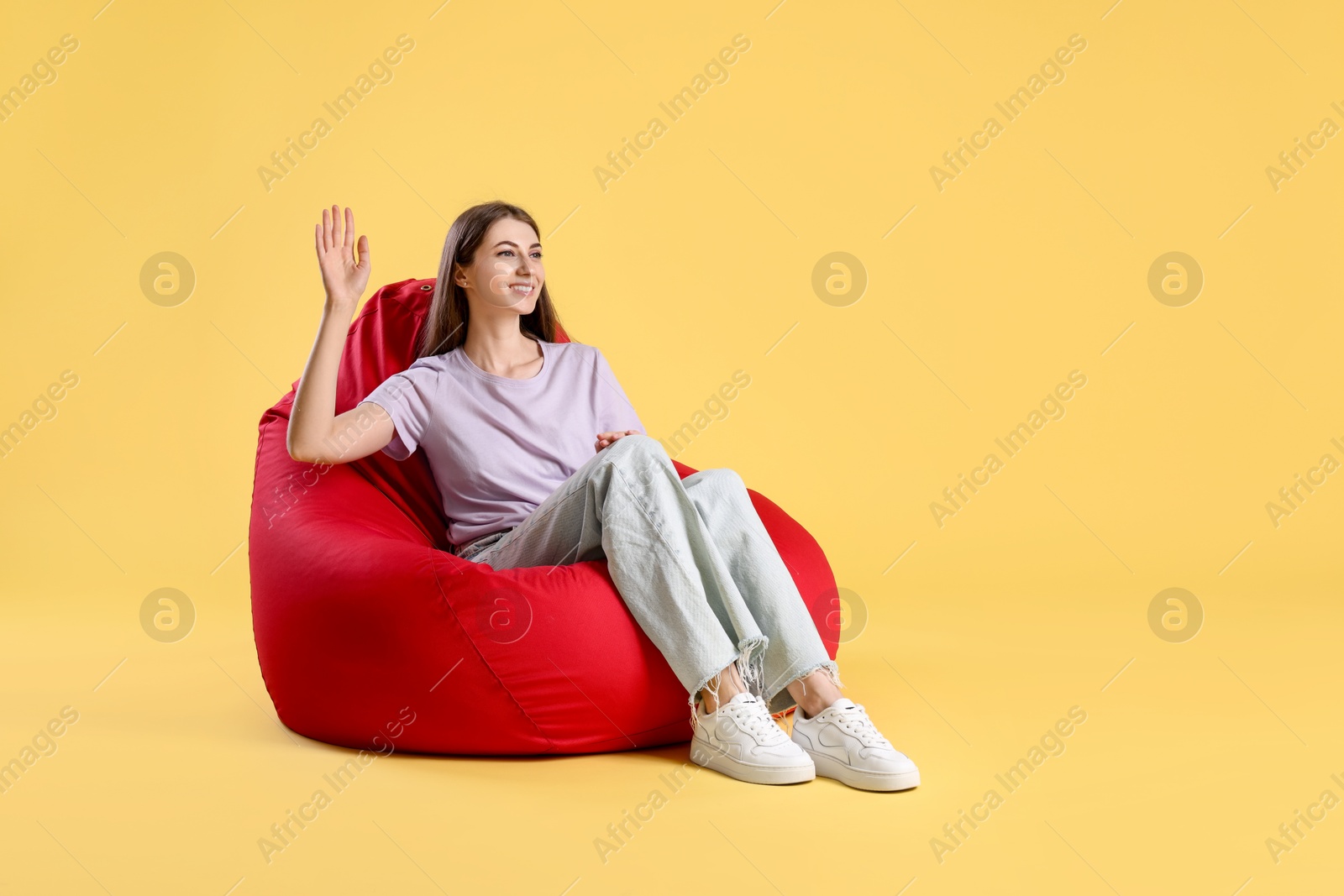 Photo of Smiling woman sitting on red bean bag chair against yellow background, space for text