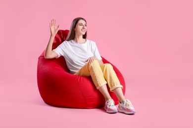 Photo of Smiling woman sitting on red bean bag chair against pink background, space for text