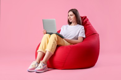 Photo of Beautiful young woman using laptop on red bean bag chair against pink background