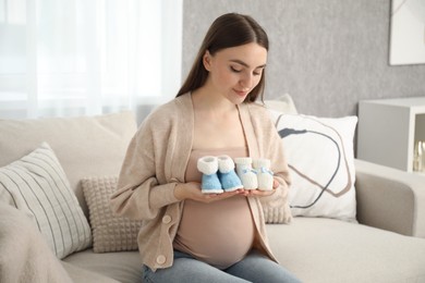 Photo of Expecting twins. Pregnant woman holding two pairs of shoes at home