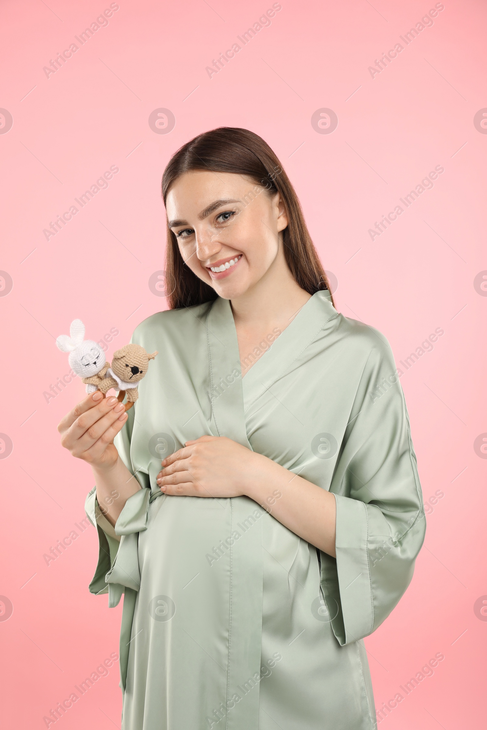 Photo of Expecting twins. Pregnant woman holding two toys on pink background